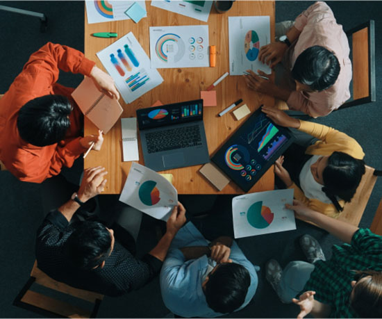 A diverse group of individuals collaborating around a table, each engaged with their laptops.