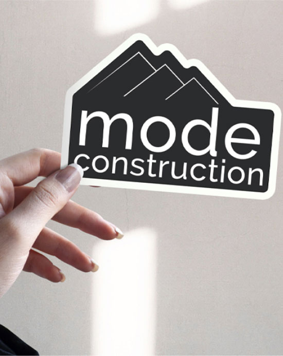 A person displays a sticker that reads mode construction, emphasizing a theme of building or development.