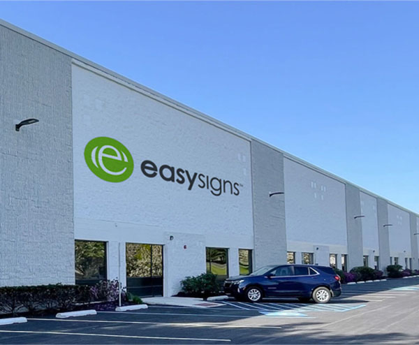 A view of the Easy Signs building located in a parking lot, showcasing its exterior and surrounding vehicles.