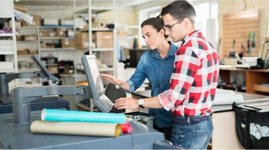 Two individuals collaborating on a computer inside a warehouse environment.