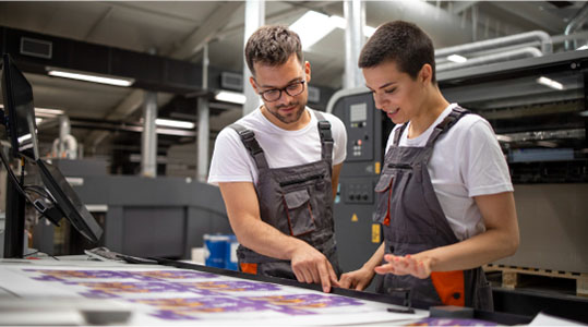 Two colleagues collaborating in an office setting, focused on a large print displayed prominently in the workspace.