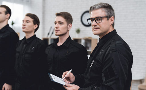 Five men in black uniforms standing in a line, displaying a unified and disciplined appearance.