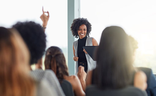 A woman stands confidently at the front, presenting to an engaged audience of diverse individuals.