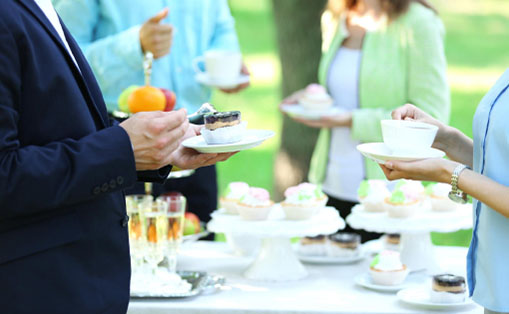 A group of individuals gathered around a table filled with various food and drinks, enjoying a social occasion together.