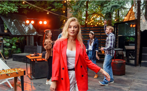 A woman in a red coat stands confidently in front of a diverse group of people, engaging in conversation.