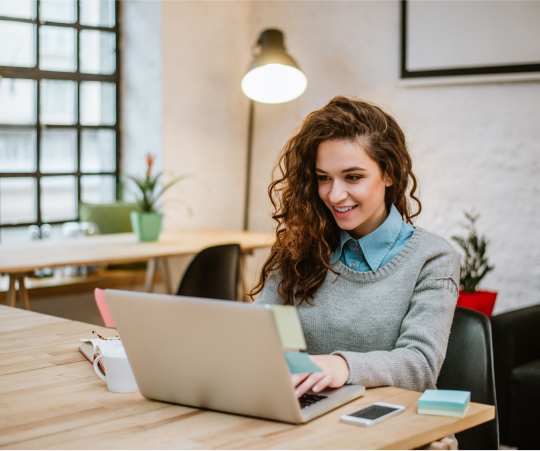 A woman seated at a table, focused on her laptop, engaged in work or study.