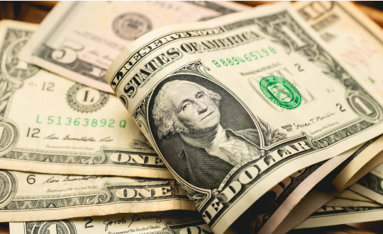 A stack of U.S. dollars neatly arranged on a wooden table, showcasing the currency's distinct green and white design.