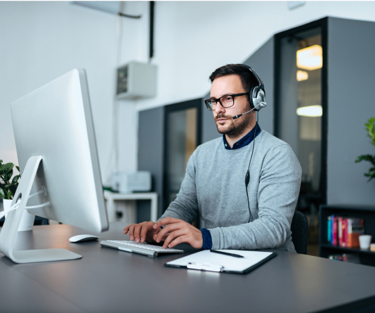 A man with headphones and glasses is seated at a desk, focused on his work or listening to audio.