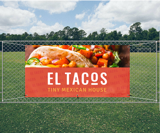 A sign for El Tacos displayed on a fence amidst a grassy field.