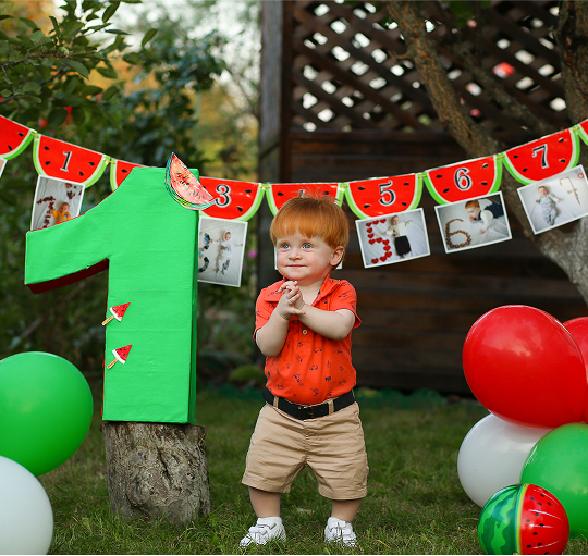 A boy stands proudly in front of a vibrant watermelon banner, showcasing a cheerful summer theme.