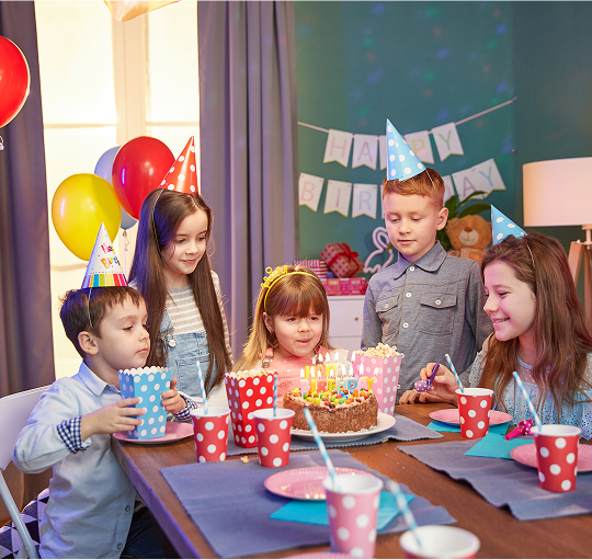 A joyful group of children celebrating together at a colorful birthday party, surrounded by balloons and cake.