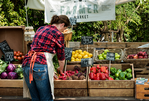 A woman stands before a table adorned with an array of fresh fruits and vegetables.