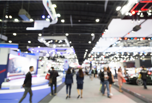 Blurry image of individuals navigating through a bustling indoor exhibition space.