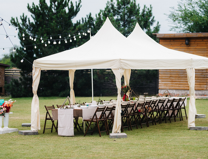 A beautifully decorated tent set up for an elegant wedding reception, adorned with lights and floral arrangements.