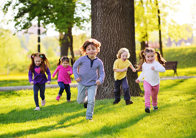 Children joyfully running through a vibrant park, surrounded by greenery and bright flowers, enjoying a sunny day.