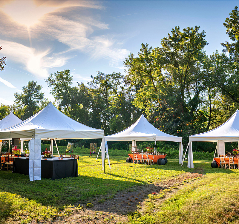 A large white tent is set up outdoors, ready for an event, surrounded by green grass and trees in the background.