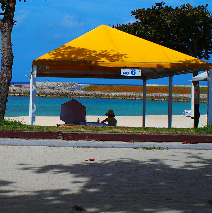 A person sitting on the beach under a bright yellow canopy, enjoying the sun and the ocean view.