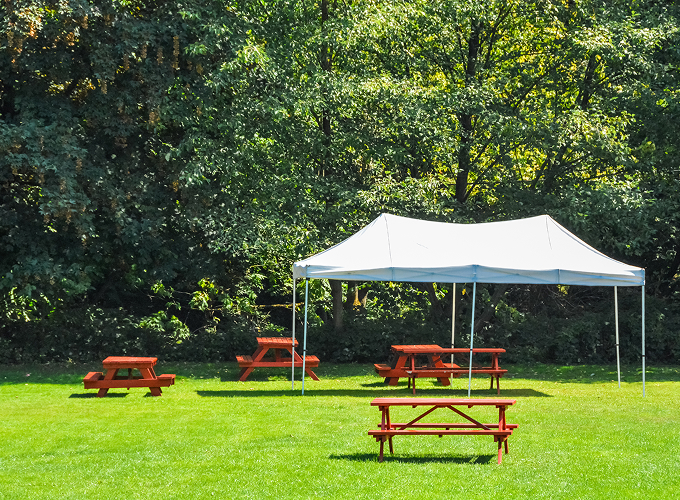 A tent set up in the center of a grassy field, surrounded by open space and a clear blue sky.