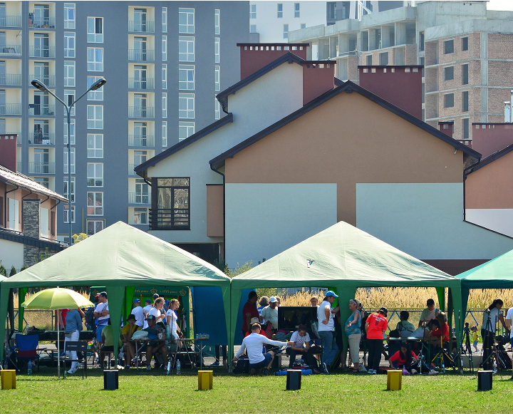 A group of people gathered and sitting together under a large green tent, enjoying a social event outdoors.