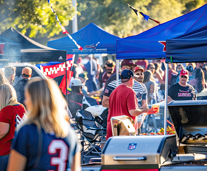 A diverse group of people enjoying a barbecue outdoors, smiling and socializing around a grill and picnic table.