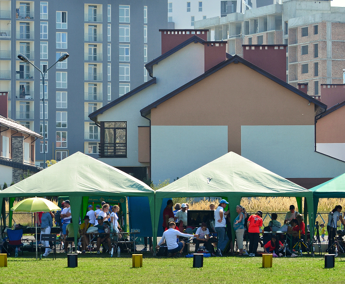 A diverse group of people seated together under a large green tent, engaged in conversation and enjoying their time.