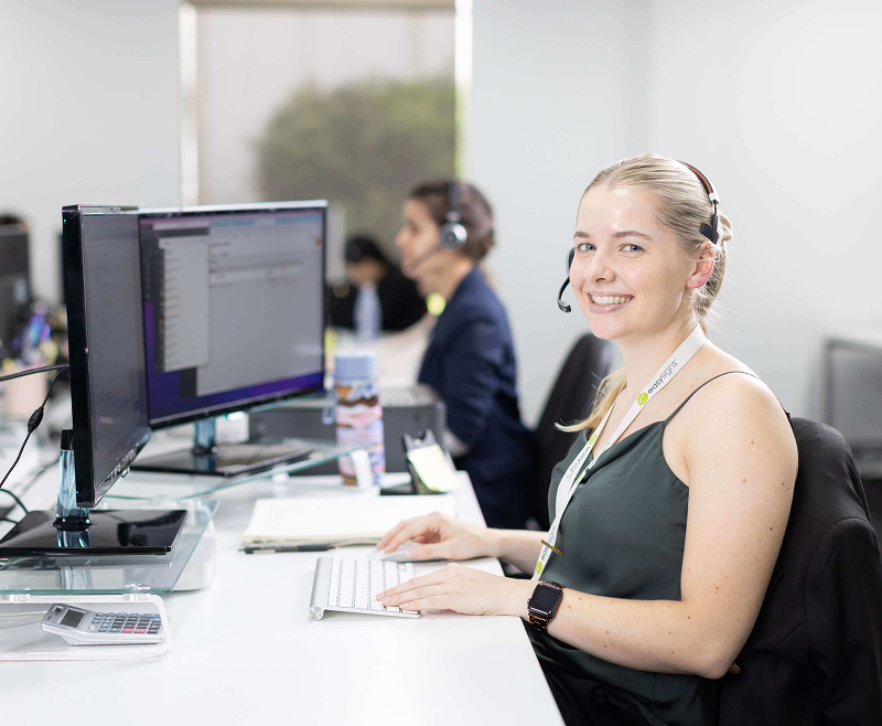 A woman seated at a desk, focused on work, with two computer monitors displaying various applications.