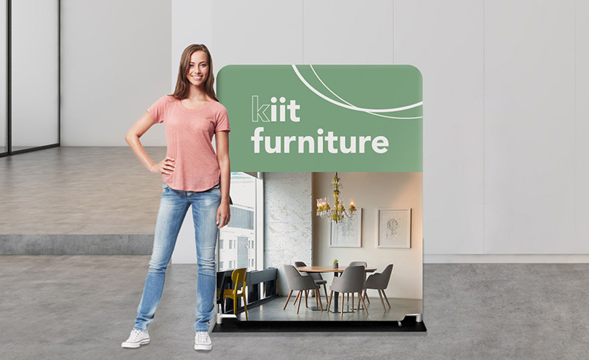 A woman stands beside a large banner displaying the words 'Lift Furniture.'