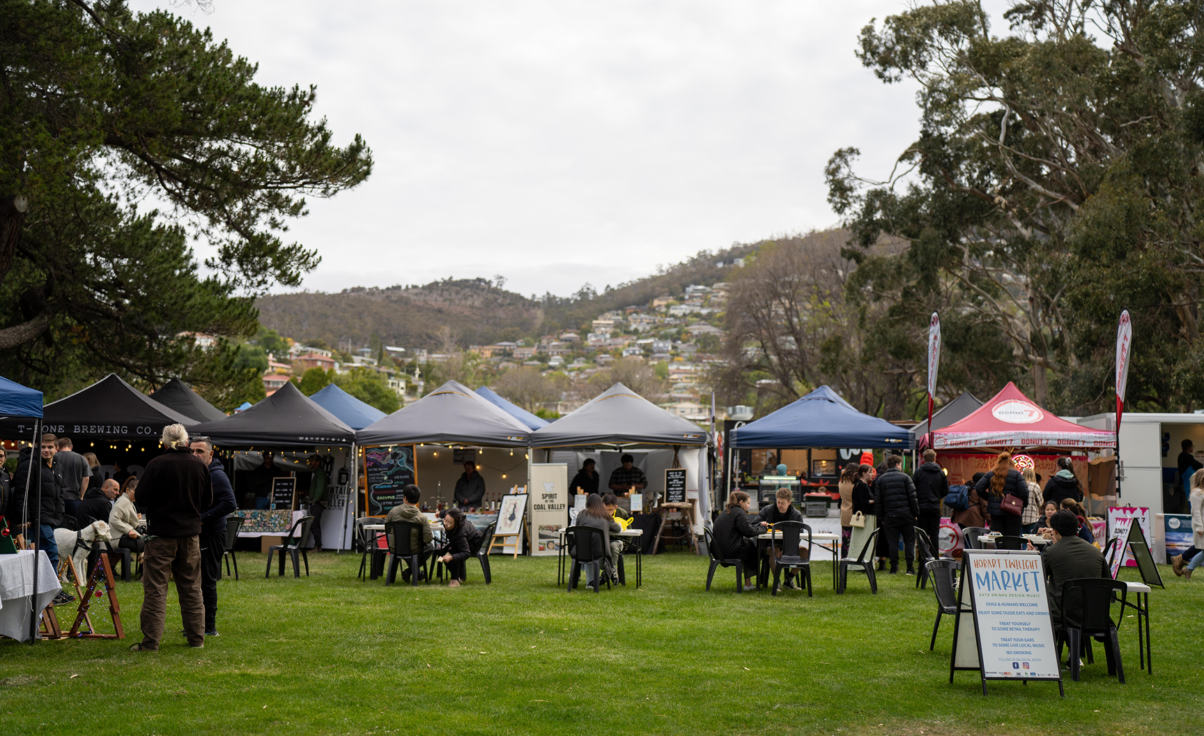 People seated at tables in a bustling outdoor market, surrounded by various stalls and vibrant displays of goods.